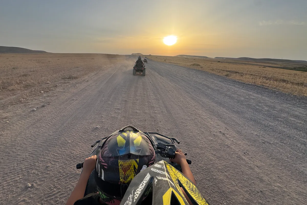 Sur un quad, derrière un pilote casqué, on suit deux autres quads sur une large piste face au soleil bas, désert d'Agafay (juin 2026)