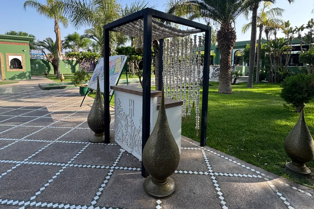 Un comptoir blanc sculpté de feuillages et du monogramme JH, entre des lampes en métal doré ajouré, au Jardin de l'Hivernage (juin 2026)