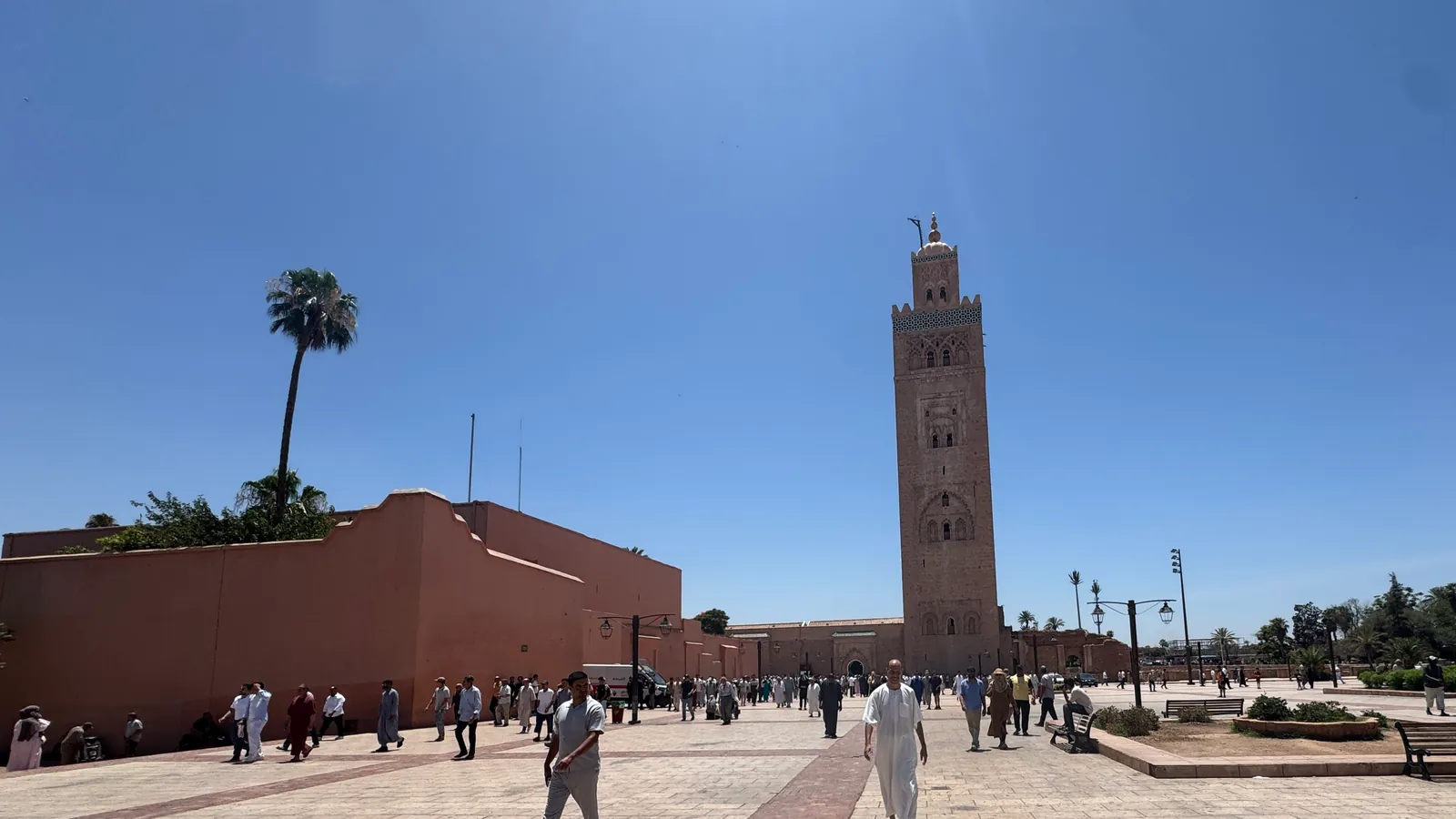 Worshippers crossing the Koutoubia esplanade as they leave Friday prayers; in the background, the minaret under a cloudless sky