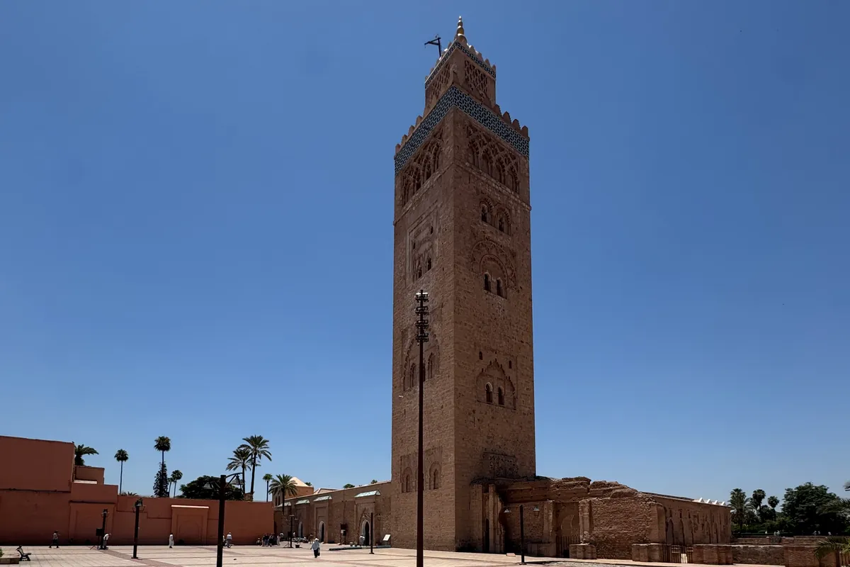 Le minaret de la Koutoubia vu de l'esplanade, entre le mur de la mosquée à gauche et des murs en ruine à droite (juin 2026)