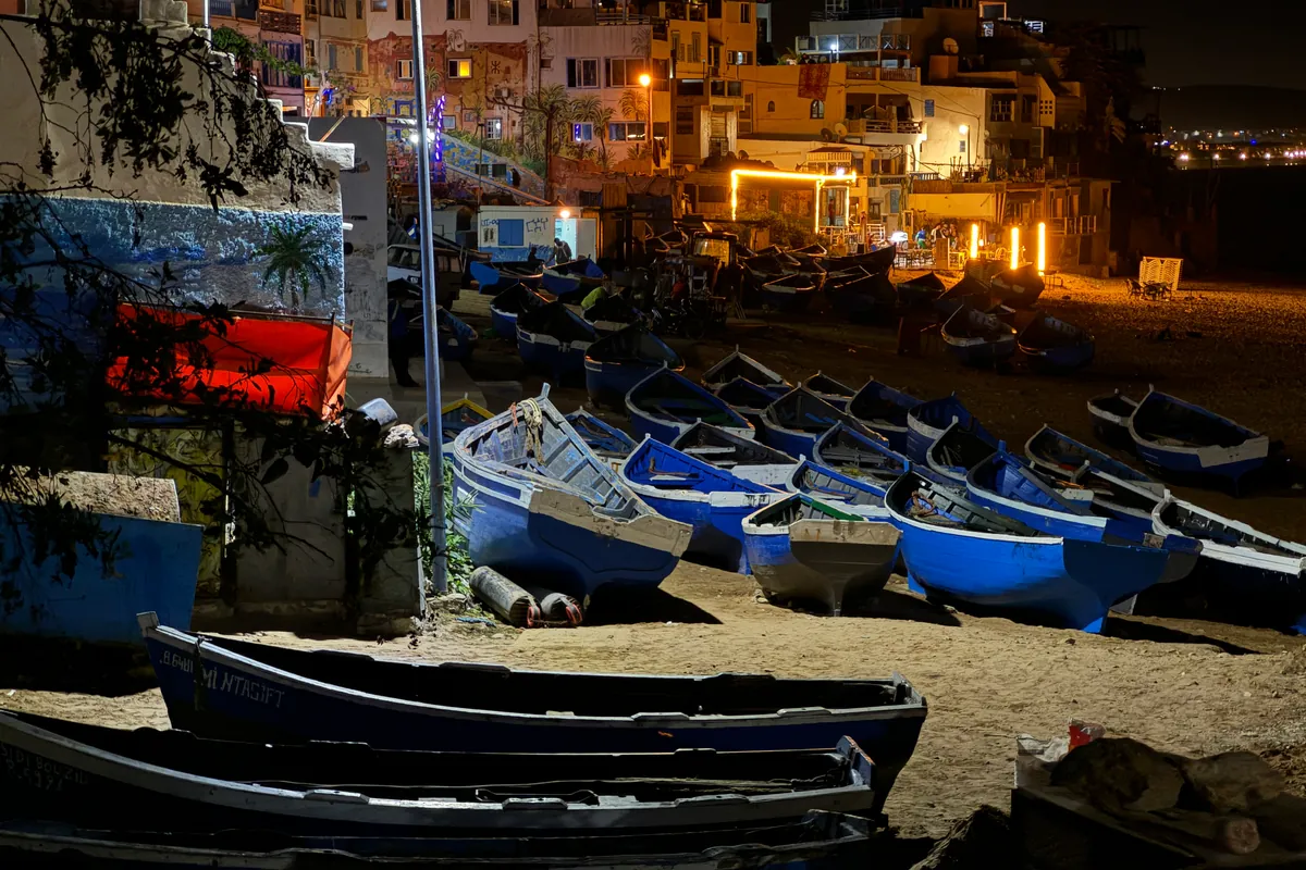 Les barques bleues des pêcheurs tirées sur le sable, au pied des maisons éclairées de Taghazout, à la nuit tombée (octobre 2024)