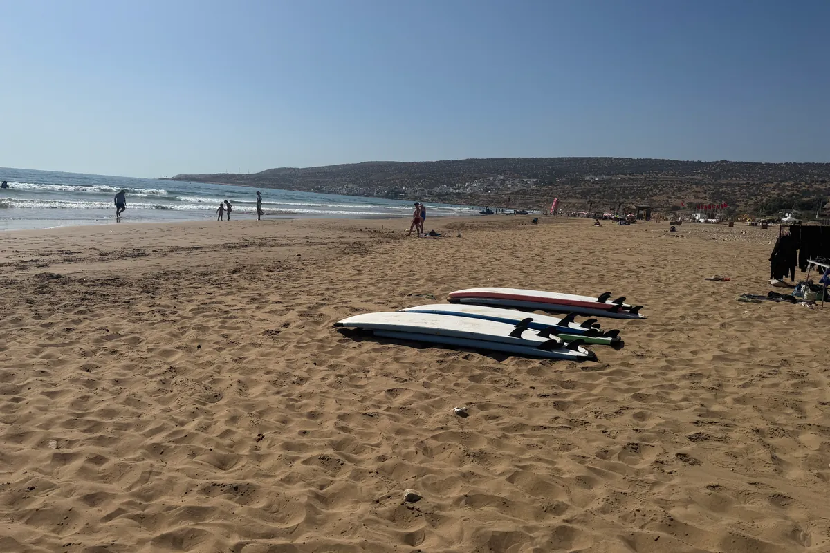 Six planches de surf posées à l'envers sur le sable de la grande plage, au sud-est de Taghazout (mai 2026)