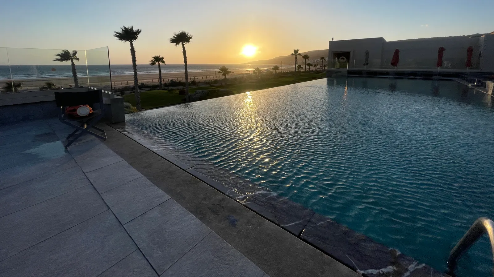 El sol poniéndose sobre la playa, más allá de una piscina infinita y de palmeras, en el Riu Palace Tikida Taghazout