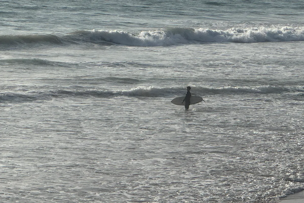 Un surfeur entre dans l'eau, planche sous le bras, à Taghazout (octobre 2025)