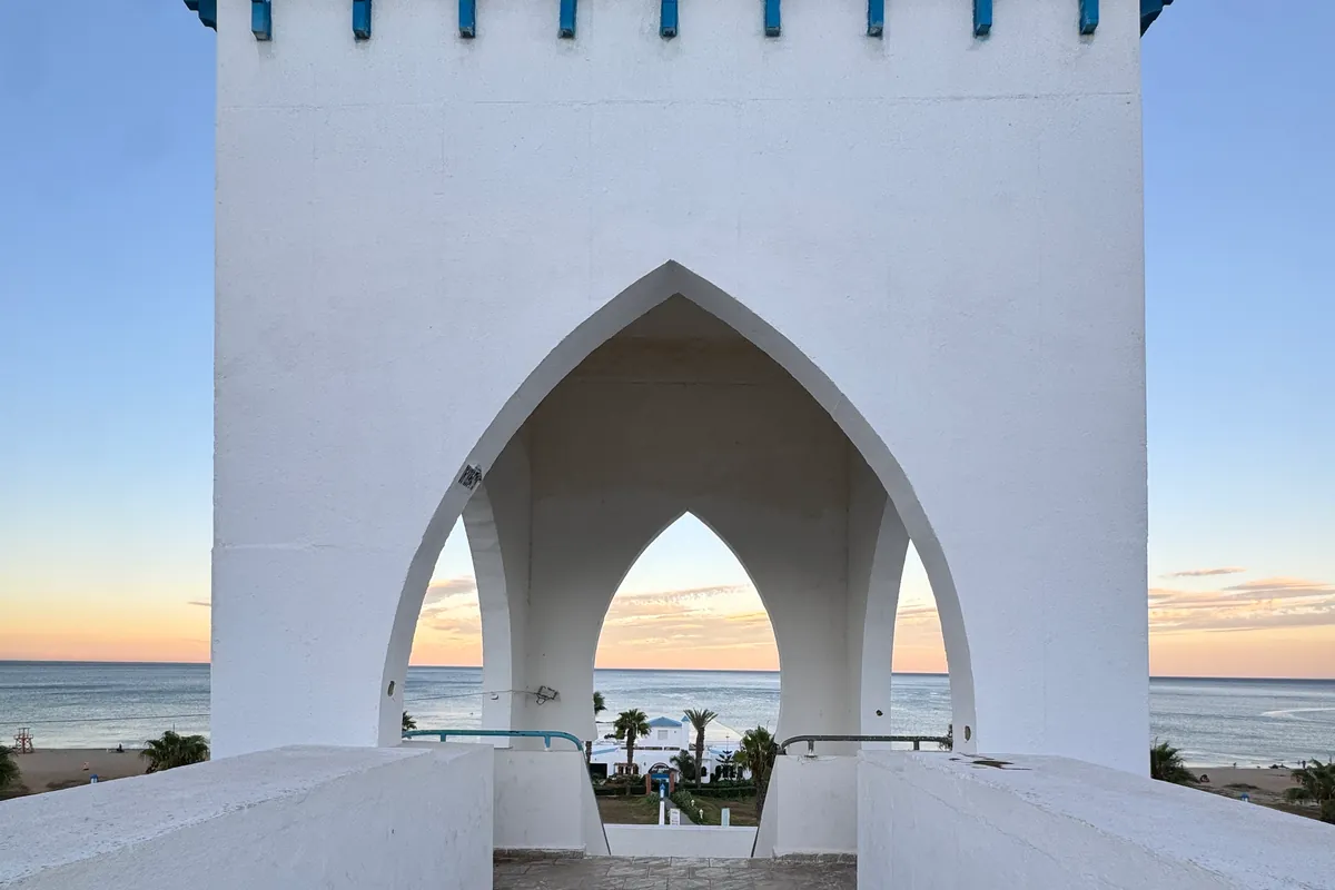 La mer et le ciel rosé du soir à travers les arches en ogive de la tour de la passerelle, face à la plage Riffiine (septembre 2026)