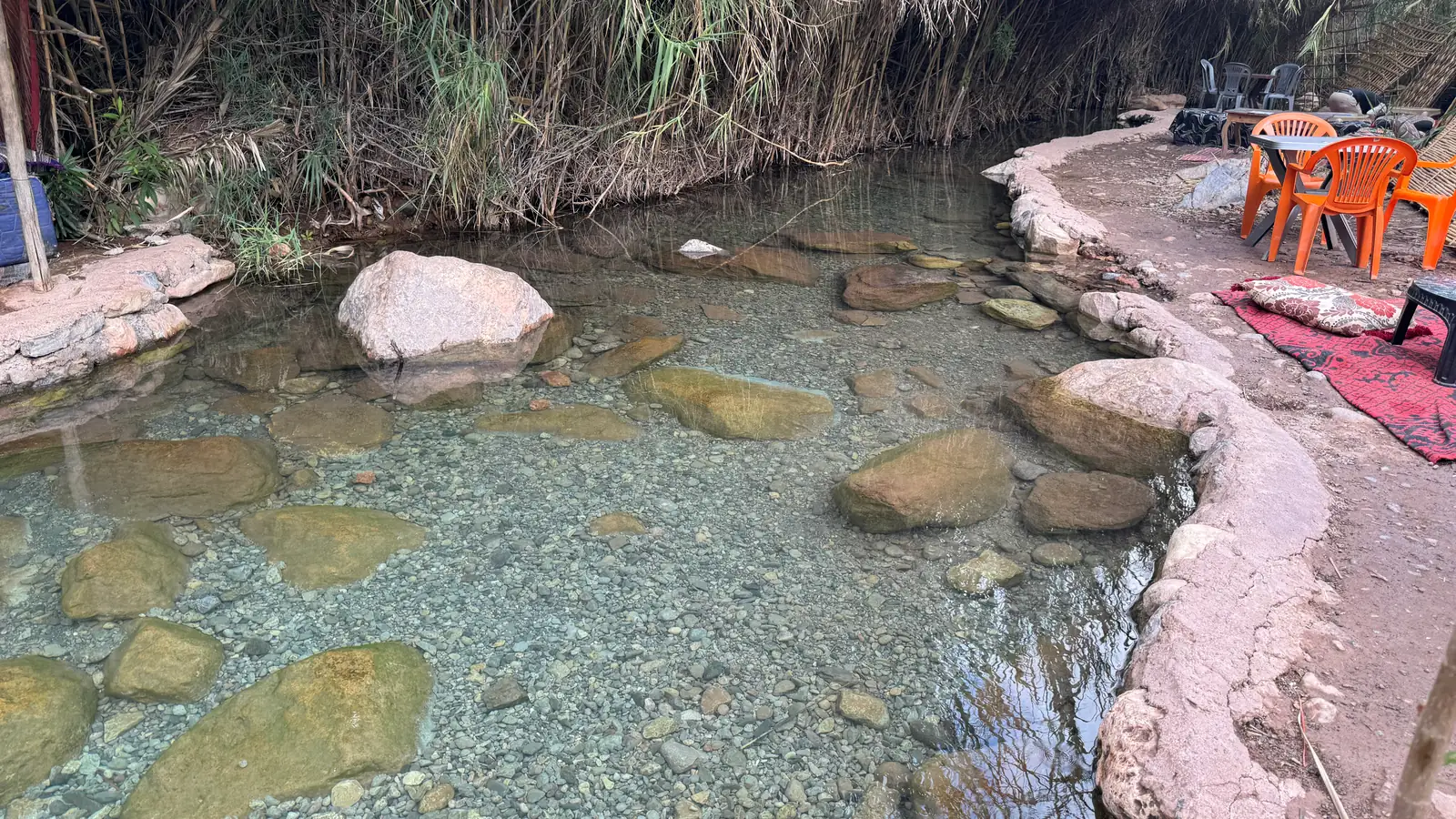 Une vasque d'eau claire entre les rochers, avec les chaises orange d'un café au bord