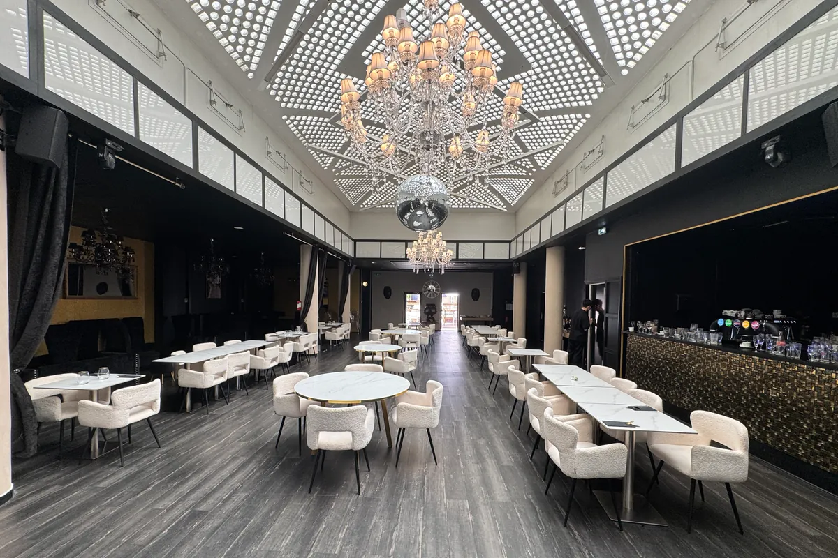 La grande salle du Z sous un plafond lumineux à motifs, avec des lustres à pampilles, une boule à facettes, des tables blanches et des fauteuils clairs (juillet 2026)