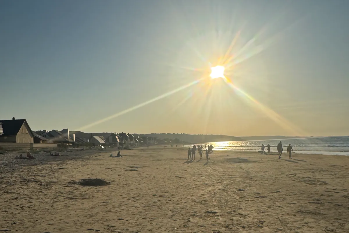 Des promeneurs en silhouette sur la grande plage d'Urville-Nacqueville, face au soleil du soir (août 2026)