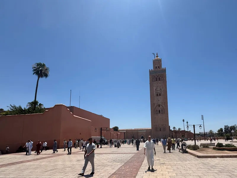 Fieles cruzan la explanada de la Kutubía a la salida de la oración del viernes; al fondo, el alminar, bajo un cielo sin nubes