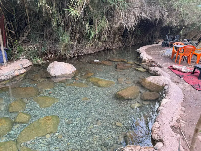 Une vasque d'eau claire entre les rochers, avec les chaises orange d'un café au bord
